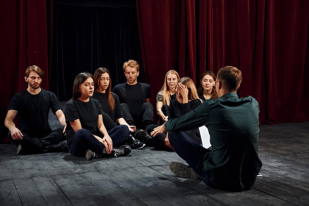 Sitting on the floor Group of actors in dark colored clothes on rehearsal in the theater