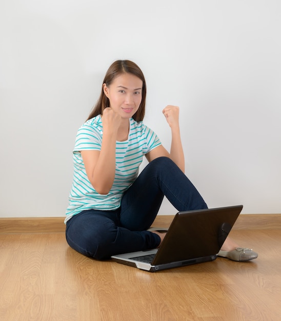 Seduto per terra con un portatile alzando le braccia con uno sguardo di successo