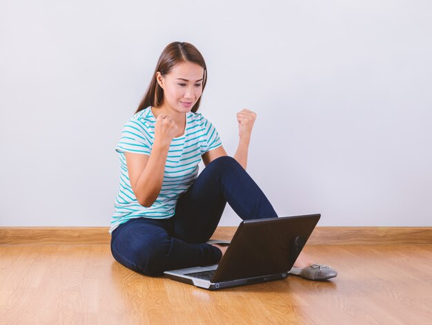 Sitting on the floor with a laptop raising his arms with a look of success