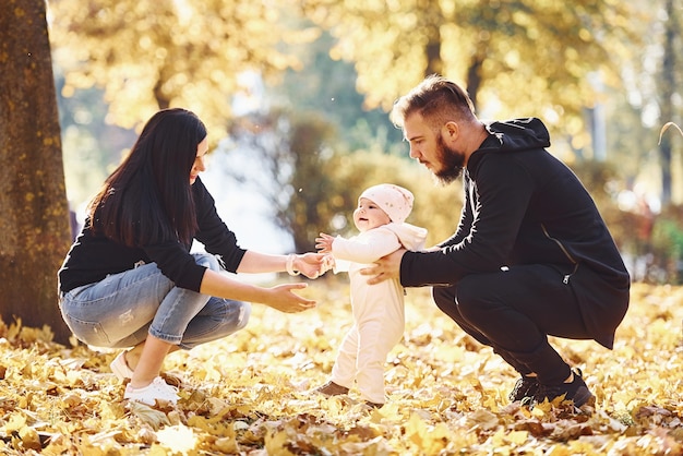 Sitting on the ground. Cheerful family having fun together with their child in beautiful autumn park.