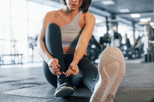 Sitting on the ground woman in sportive clothes with slim body\
type is in the gym