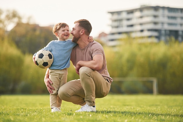 Sitting holding soccer ball Happy father with son are having fun on the field at summertime