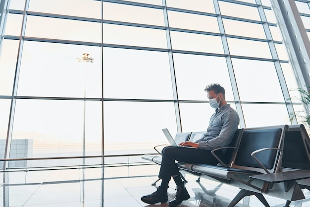 Sitting inside Young man in formal wear is in modern airport Conception of vacation