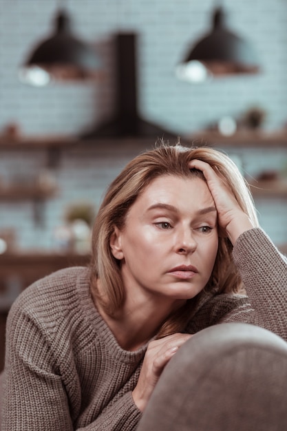 Sitting in kitchen. Blonde-haired businesswoman sitting in the kitchen at home having some problems