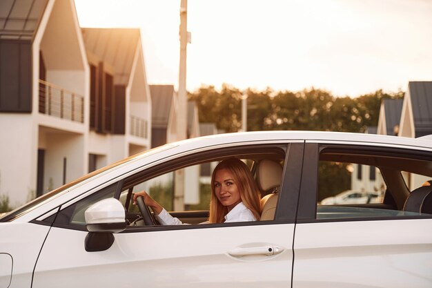 Sitting and looking at the camera Young woman in white clothes is with her electric car at daytime