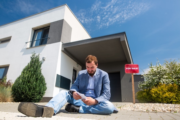 Sitting man without work in front of the house during economic crisis, selling real estate