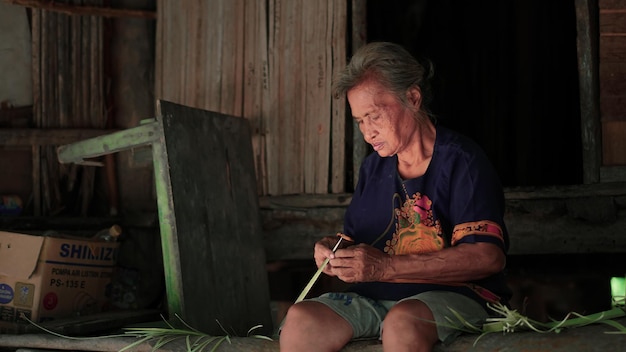 sitting old woman making palm leaf knitting