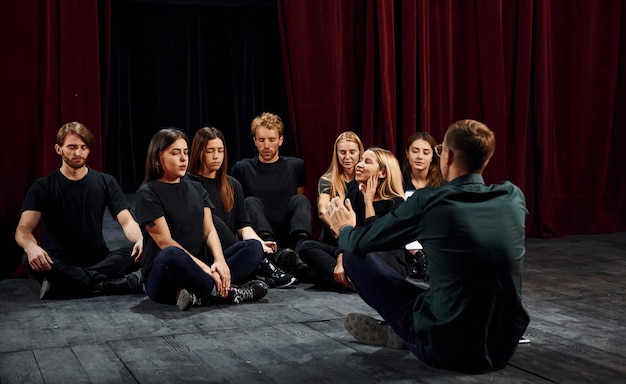Фото Сидя на полу группа актеров в темной одежде на репетиции в театре