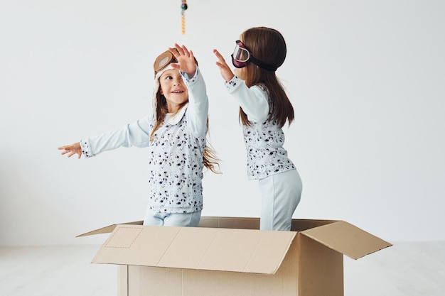 Sitting in the paper box Two cute little girls indoors at home together With retro pilot glasses and hat