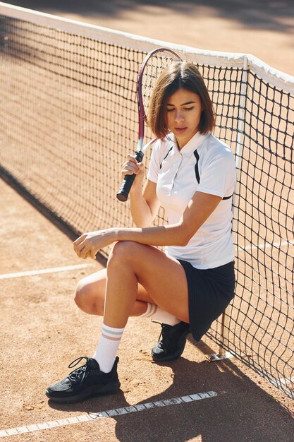 Sitting and posing Female tennis player is on the court at daytime