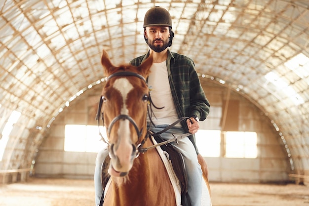 Photo sitting in the saddle young man with a horse is in the hangar