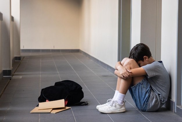 sitting in school hallway boy hugging knees with backpack and notebooks nearby