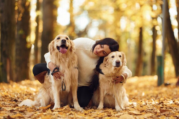 Foto seduta e sorridente donna sulla passeggiata con i suoi due cani nella foresta autunnale