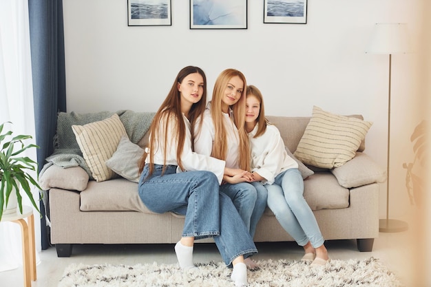 Sitting on the sofa Young mother with her two daughters at home at daytime