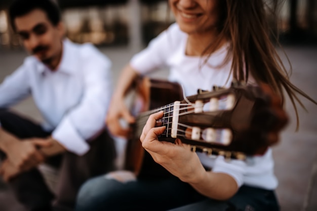 Foto seduto sulle scale e suonare la chitarra. ragazza che gioca chitarra mentre sedendosi con il suo amico maschio all'aperto nella città.