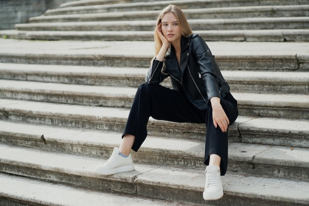 Sitting on the steps in a fashionable black stylish clothes and posing for the camera portrait