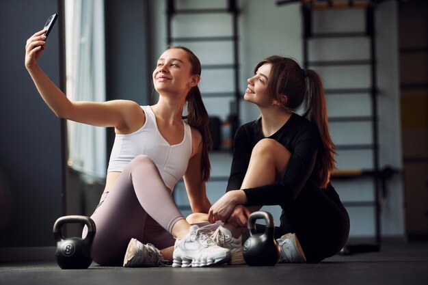 Sedersi e fare una pausa due donne in abiti sportivi trascorrono insieme una giornata di fitness in palestra