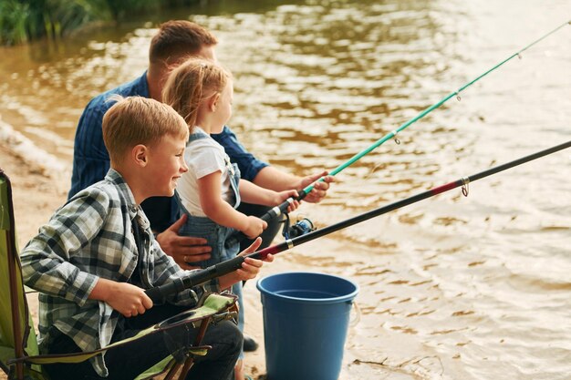 Sitting together Father with son and daughter on fishing outdoors at summertime