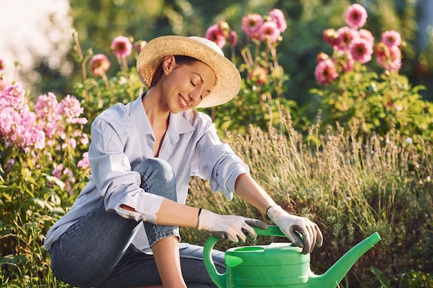 Sitting with watering can Young cheerful woman is in the garden at daytime