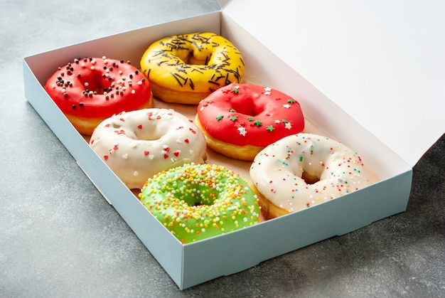 Photo six assorted glazed sweet donuts in a paper box on a table