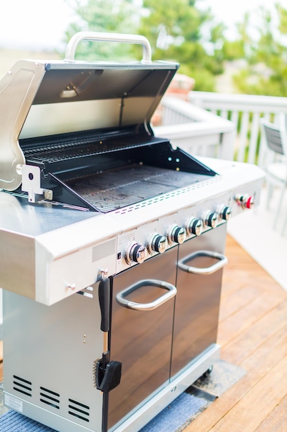 Six burner outdoor gas grill with open lid on backyard.