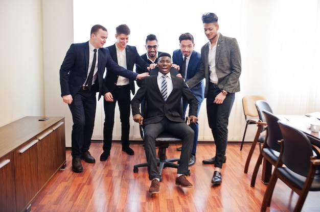 Six business men standing at office and man on chair