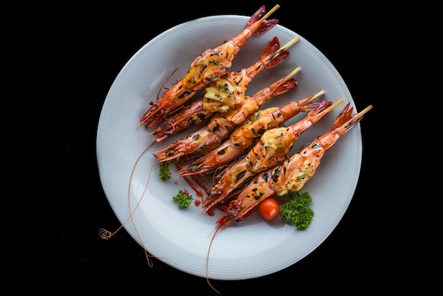 Six grilled shrimps with cheese on blue plate isolated on black background top view