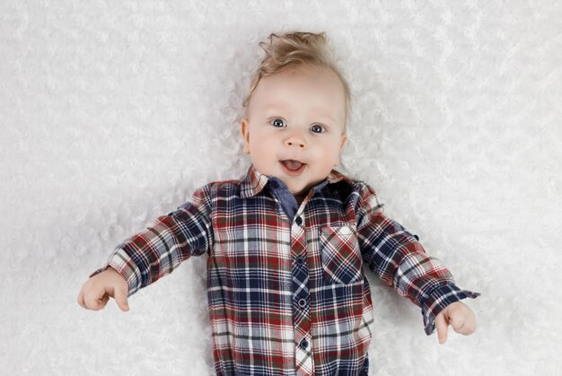 A six-month-old blond boy with blue eyes in a plaid shirt lies, smiling cute,