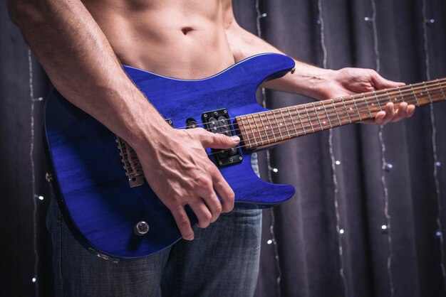 파란색 일렉트릭 기타와 함께 포즈를 취하는 식스팩 남자. 록 콘서트 개념입니다. 혼합 매체