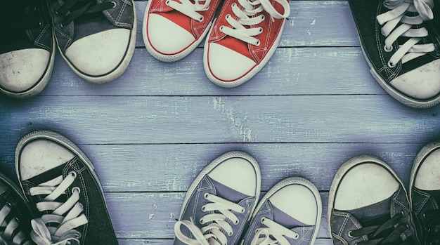 Six pairs of old, worn sneakers on lilac wooden surface