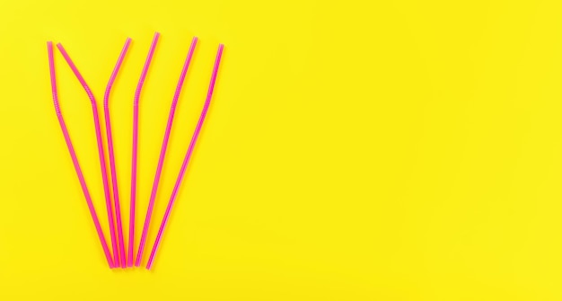 Six pink plastic drinking straws on yellow board, view from above, space for text right side