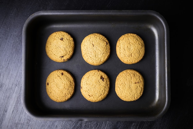 Six round baked cookies on a black baking sheet, view from above