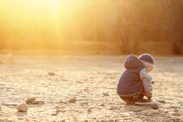 A six-year-old boy with autism sits on the ground alone at sunset. 