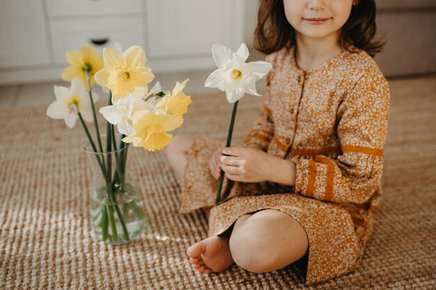 写真 床の上に座って黄色の水仙の花を持つ 6 歳の女の子