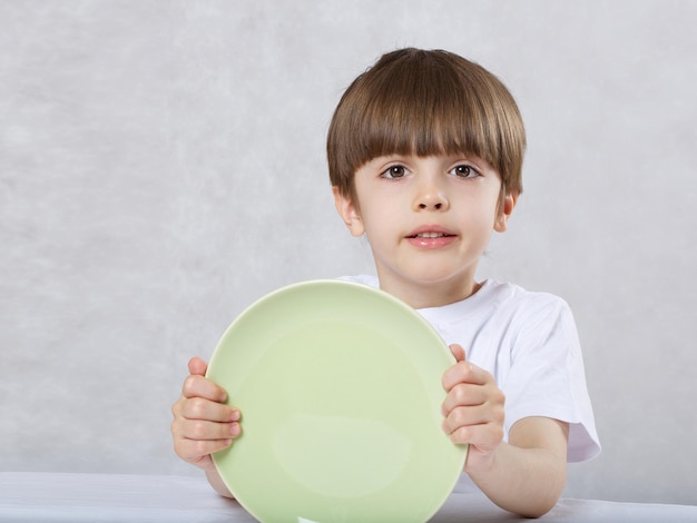 空の緑のプレートを持つ6歳の少年。テキスト用の空き容量。