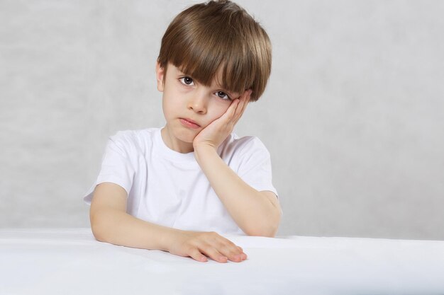 Six years old child in white t-shirt at the table. Closeup