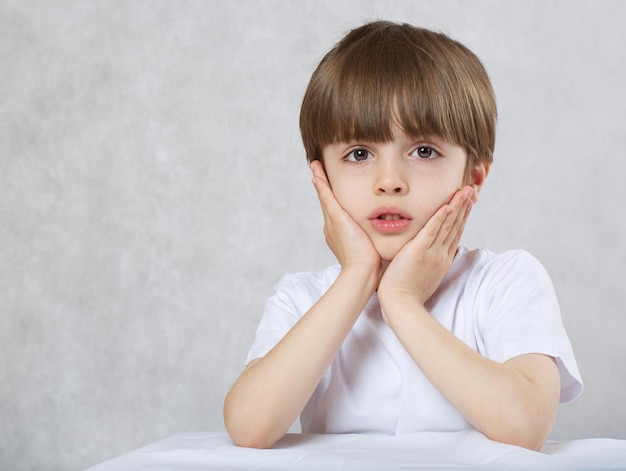 Six years old child in white t-shirt at the table. Closeup