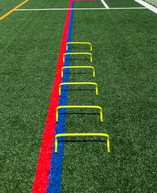 Photo six yellow mini hurdles lined up in a straight line on a turf field for speed and agility training