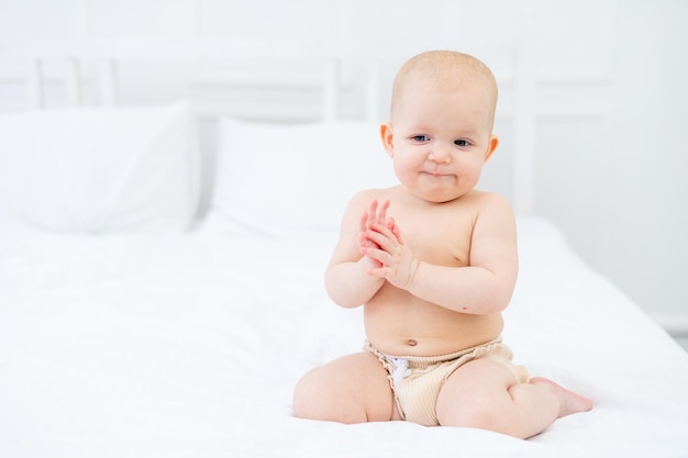 A sixmonthold baby in diapers on a white cotton bed at home playing and smiling