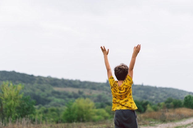 A sixyearold boy is standing with his back in the countryside Back view Happy child boy laughing and playing in the summer day