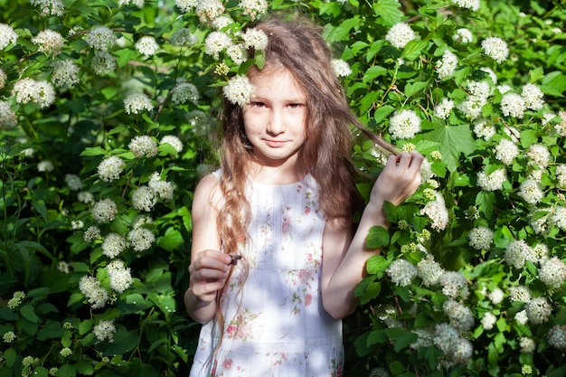 꽃이 만발한 관목에 긴 머리를 한 6세 소녀