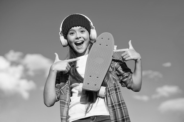 Skateboard you can trust Happy girl pointing at penny board Little skater with pointing gesture on blue sky Pointing for advertising Marketing and promotion Good for transportation copy space