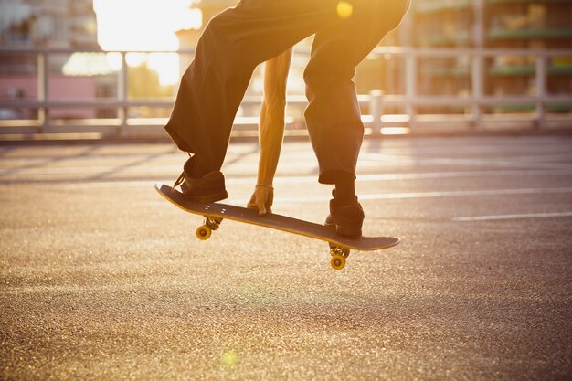 街の通りでトリックをしているスケートボーダー、クローズアップの瞬間。スニーカーとキャップに乗ってアスファルトでスケートボードをしている若い男。余暇活動、スポーツ、エクストリーム、趣味、運動の概念。