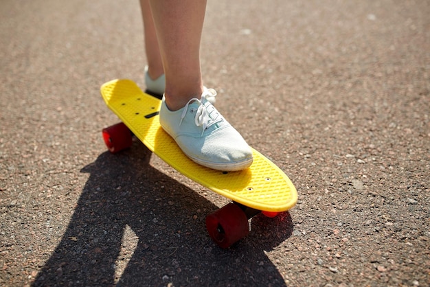 skateboarding, leisure, extreme sport and people concept - close up of teenage girl legs riding short modern cruiser skateboard on road