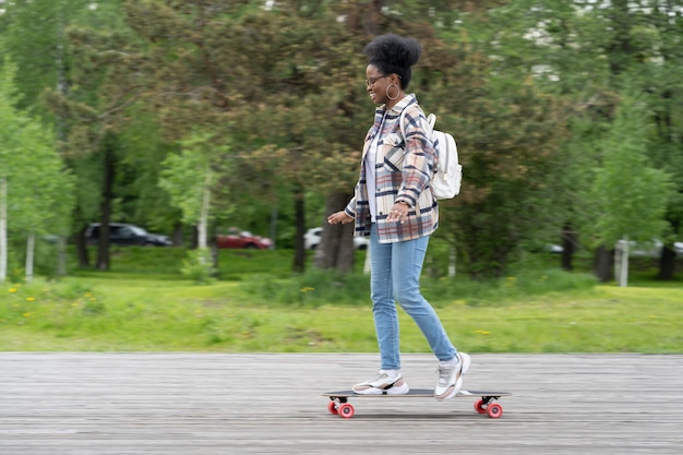 도시 공원에서 롱보드를 타고 스케이트보드와 도시 생활을 하는 트렌디한 캐주얼 젊은 아프리카 여성