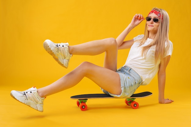 Skateborder meisje in korte broek en T-shirt aan boord zitten over geel
