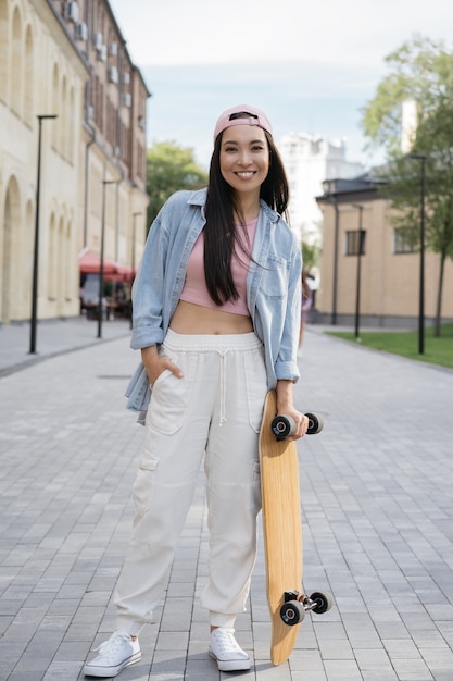 Skater girl holding skateboard posing for pictures outdoors