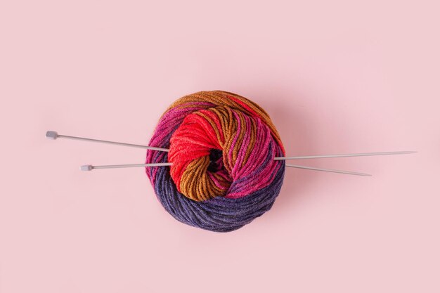 A skein of colored woolen threads and knitting needles on a pink background selective focus