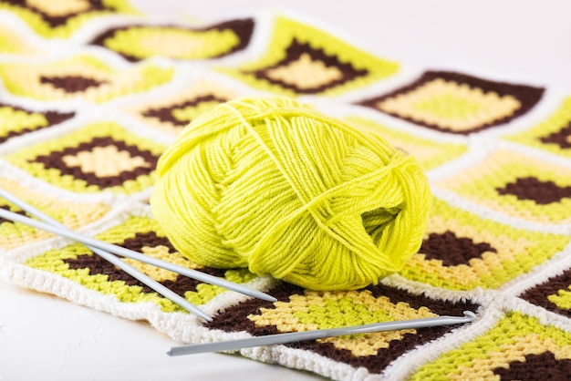 A skein of green threads with a crochet hook and knitting\
needles on the background of a patchwork