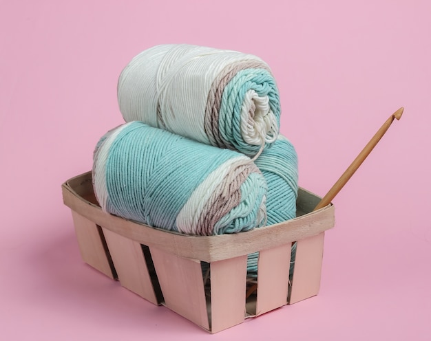 Skein of woolen threads of pastel colors and crochet hook in basket
